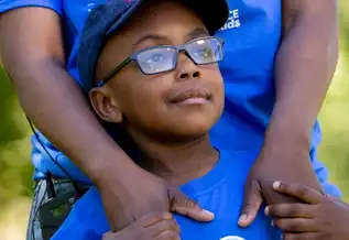 A young boy, Malembo, stands in front of his parent and holds their hands