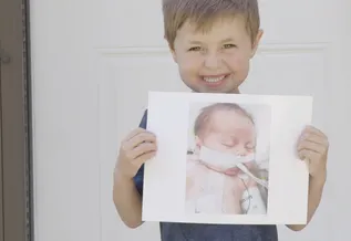A young patient, Presley, grins while holding a photo of himself as a baby when he was undergoing treatment at BCH