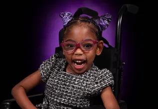 young girl smiling in pink glasses on a wheelchair